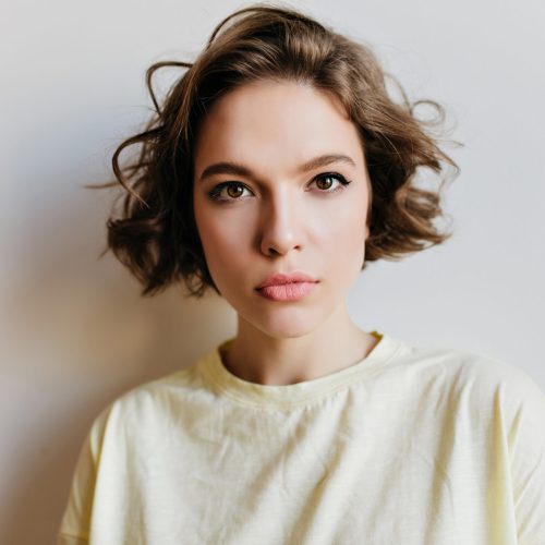 Close-up portrait of fascinating serious girl isolated on white background. Spectacular european female model with curly hairstyle looking to camera.